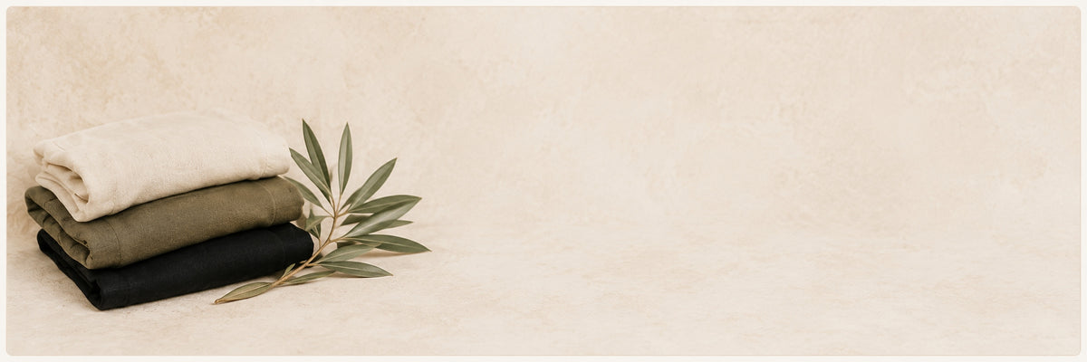 Folded beige apparel with green palm leaves on a warm neutral background for Hashem faith-inspired clothing.