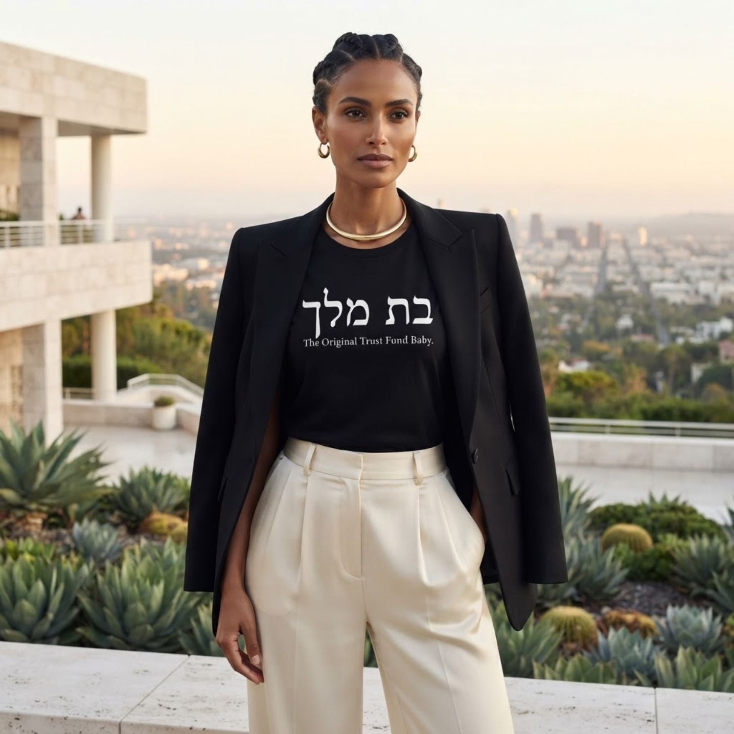 Woman wearing The Original Tee in black by Hashem Is My Sugar Daddy, featuring בת מלך and The Original Trust Fund Baby graphic styled with a black blazer and cream trousers.