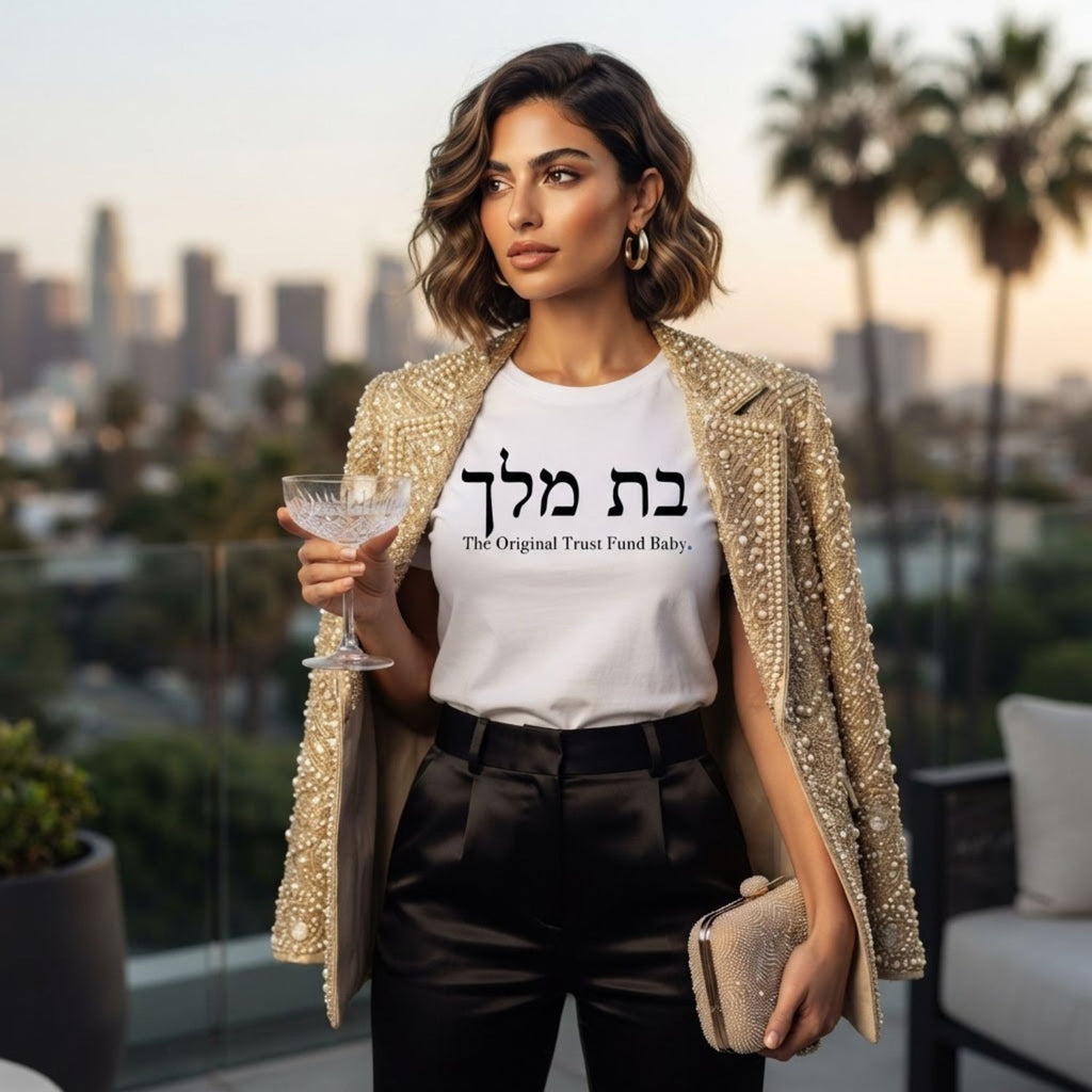 Woman wearing The Original Tee in white by Hashem Is My Sugar Daddy, featuring בת מלך and The Original Trust Fund Baby graphic styled with an elegant jacket and black trousers.