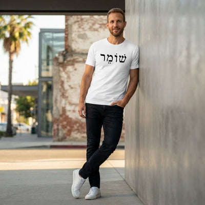 Male model wearing The Protector Tee in white by Hashem Is My Sugar Daddy, featuring black שומר Shomer Hebrew protector lettering across the chest, styled with black jeans and white sneakers in a modern urban setting.